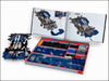 A LEGO Technic model kit set displayed on a white background, featuring a partially assembled blue and white mechanical model, an open instruction booklet showing the engine diagram, and an open storage tray filled with blue, black, and gray LEGO parts.