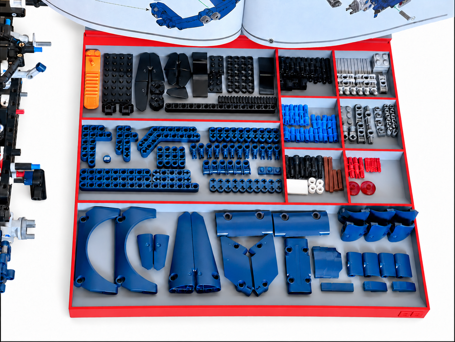 A red storage organizer filled with blue, black, gray, and orange building blocks and small parts, shown from above on a white background. An instruction booklet is partially visible at the top, and a constructed black-and-blue structure appears along the left edge.